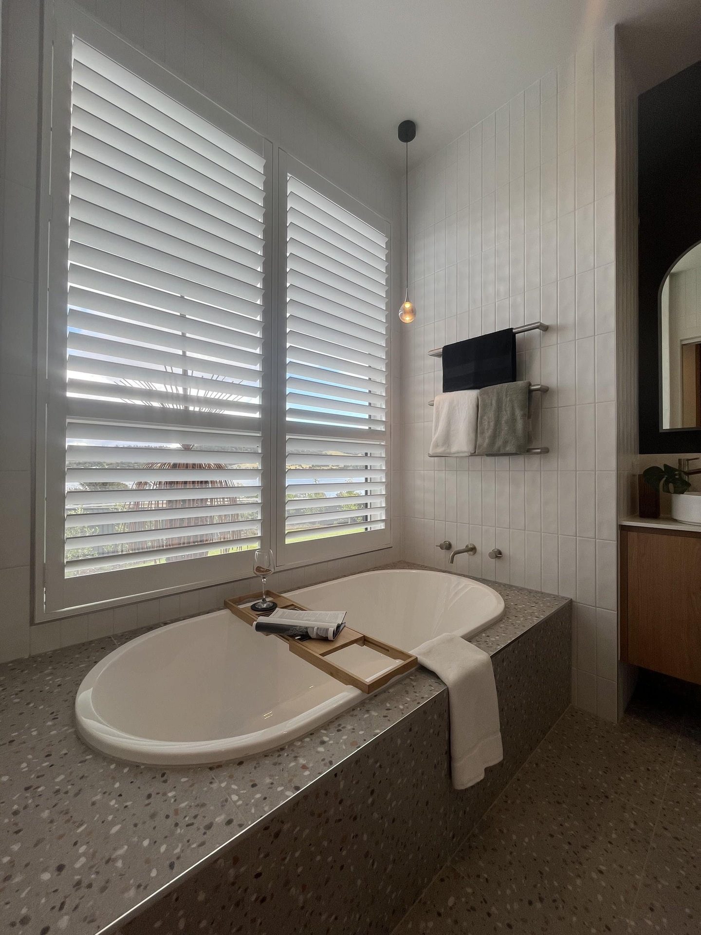 Plantation shutters around a bathtub with a stone benchtop
